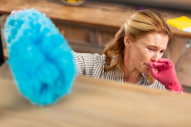 Woman In Pink Gloves Coughs While Cleaning Dusty Wooden Shelf